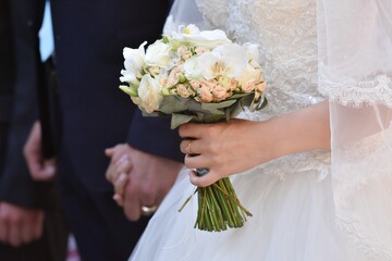 Wedding bouquet in the hands of the bride in close-up. The bride holds the groom's hand. Selective focus