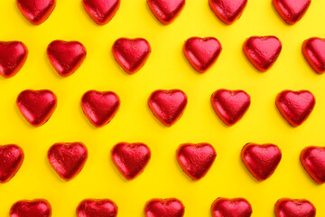 Heart shaped chocolate candies in red foil on yellow background, flat lay