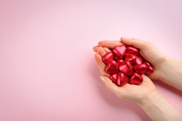 Woman holding heart shaped chocolate candies on pink background, top view. Space for text
