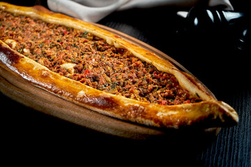 Turkish pide with minced lamb, tomatoes, bell pepper served on wooden tray. black background