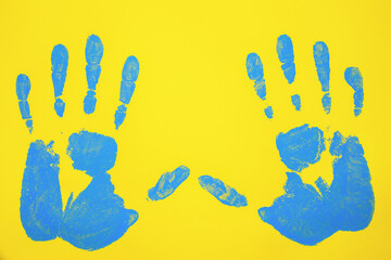 Blue handprints on a yellow poster board background. Human hands in blue ink imprinted on paper. The national colors of Ukraine. Concept of peace