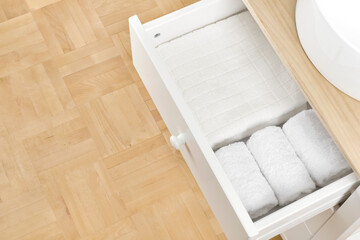 Open drawer of bathroom sink pedestal with folded white towels