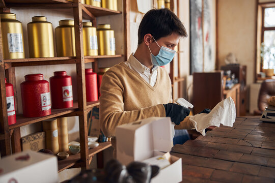 Male worker in protective face mask cleaning counter in cafe