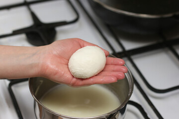 Head of mozzarella cheese in a woman's palm over the kitchen stove