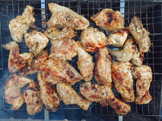 Toasty chicken marinated in mayonnaise and spices is fried on a grid over coals and smoke. The concept of outdoor recreation, picnic and lunch. Barbecue, kebab top view.