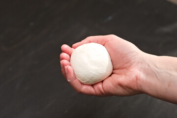 Piece of freshly made mozzarella cheese in female palm over black table