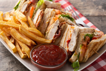 Club sandwich and French fries with ketchup sauce on wooden table	