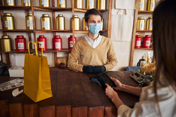Fototapeta na wymiar Young man in medical mask accepting payment from customer