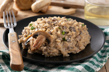 Risotto with mushroom on black plate on wooden table	