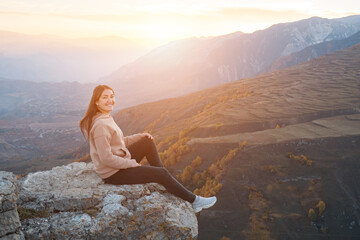 Young woman on a background of yellow trees sits on a protruding rock, sunlight.