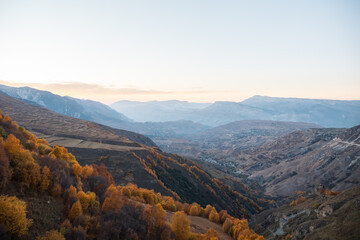 Wonderful large valley with ancient mountains covered with autumn forest and green fields under clear sky in evening panoramic view