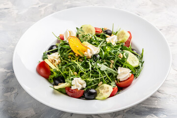 Greek salad of fresh cucumber, tomato, arugula, cream cheese, pine nuts and olives with olive oil. Healthy food, top view