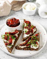 Bruschetta with cream cheese and sun-dried tomatoes. Sandwich or crostini made from wholegrain bread, cream cheese and sun-dried tomatoes. Bruschetta in a white plate on the light gray kitchen table