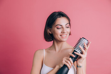 Women on pink background hold round brush hair dryer to style hair