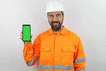 Man with beard wearing worker uniform and hardhat showing smartphone green screen