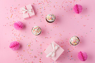 Festive gift boxes, pink paper decorations, sweet macaroons and cupcakes on pink sprinkles...