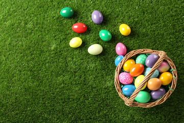 Wicker basket with Easter eggs on green grass, flat lay. Space for text