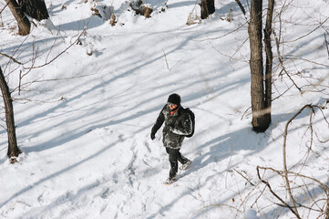 A young man, a wanderer, a tourist in black clothes with a backpack on his back walks through the snowy forest, enjoying the beautiful nature and fresh air. Photography, concept.