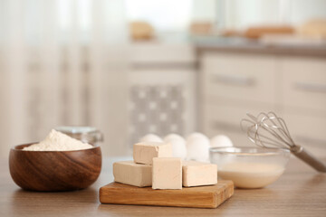 Pieces of compressed yeast and dough ingredients on wooden table indoors, space for text