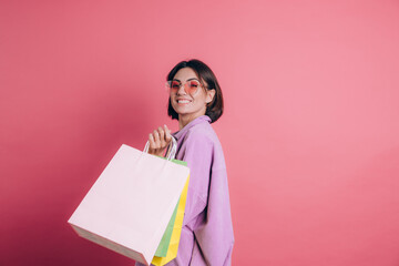 Fototapeta premium Woman wearing casual sweater on background happy enjoying shopping holding colorful bags wearing summer sunglasses