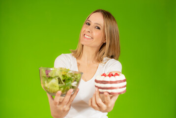 Portrait of a confused young woman choosing between cake and salads, Isolated over green background.