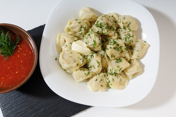 homemade dumplings in the kitchen without decorations. ready-made dumplings on a white plate, served with adjika