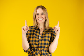 Portrait of beautiful young woman pointing up over yellow background.