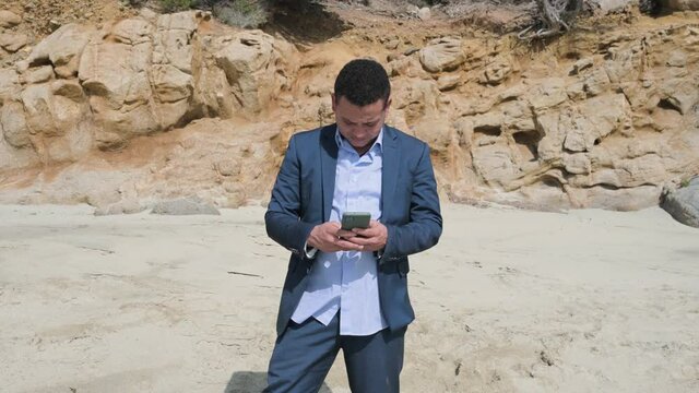 Young businessman in elegant suit standing on the beach using mobile phone. 