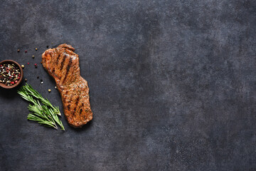 Fried beef steak with rosemary and spices on a black concrete background, top view.