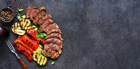Sliced fried steak and grilled vegetables with spices and rosemary on a concrete background.