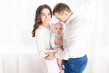 family, the concept of a happy young family with a small child, father, mother and daughter hugging at home by the window