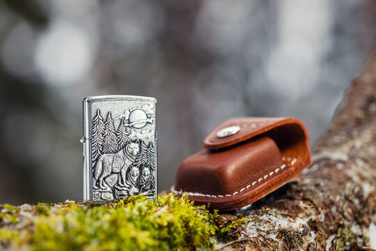Zippo Timberwolves lighter and leather case on a mossy tree trunk in a winter forest. The background is blurred.