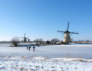 people skate on the ice near kinderdijk with al lot of windmills in holland on sunny winter day