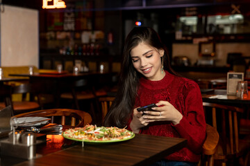 Portrait of a pretty young girl checking her phone while having lunch at the restaurant.