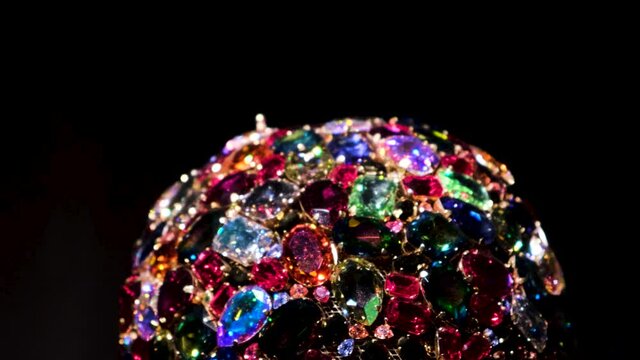Close up of amazing luxury brooch with many colorful shiny gems. Concept. Rotating jewelry shining under spotlights isolated on black background. 