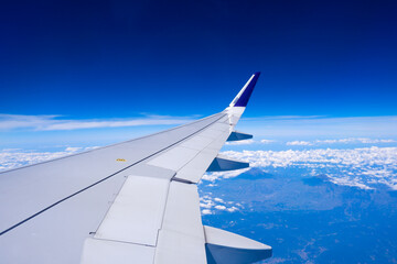 Photo of airplane wing with clouds background, horizon line and clear blue sky