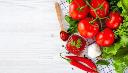 Sauce or ketchup and ingredients for his cooking: tomatoes, garlic, basil, parsley, red hot pepper and spices on a wooden white background. Close-up. Top view. Place for text.