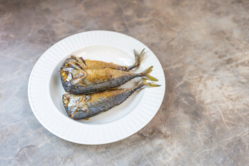 Fried mackerel fish on white ceramic plate with space on grey cement floor texture background, healthy food, easy cooking fish dish