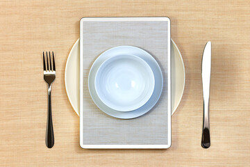Serving for one person: a plate with a fork and a knife. On top of the tablet to order food online without contact, with photos on screen of additional plates.