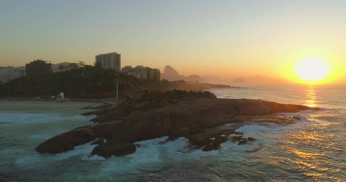 Aerial reveal of Sugarloaf Mountain from behind ocean rocks at sunrise in Rio de Janeiro