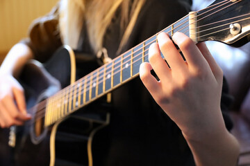 Fototapeta premium Hands of a young woman playing a black guitar. Selective focus with shallow depth of field