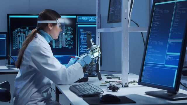 Female microelectronics engineer works in a modern scientific laboratory on computing systems and microprocessors. Electronic factory worker is testing the motherboard and coding the firmware.