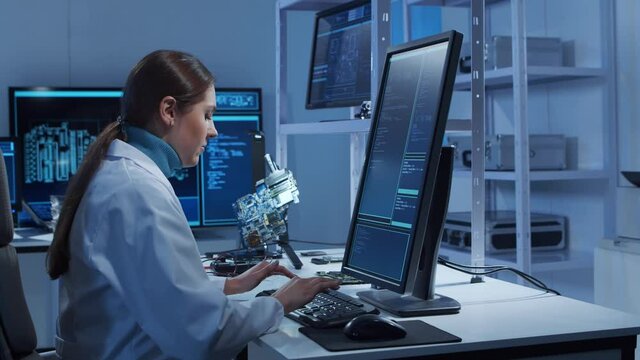 Female microelectronics engineer works in a modern scientific laboratory on computing systems and microprocessors. Electronic factory worker is testing the motherboard and coding the firmware.