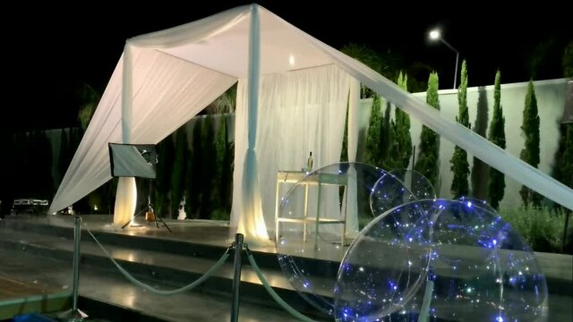 Jewish traditions wedding outdoor ceremony. Wedding canopy (chuppah, hupa) made of white fabric against the background of evening sky, palms and an artificial reservoir decorated with balloons. HD