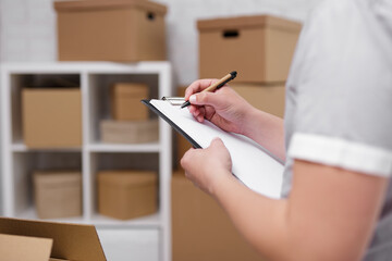 Close up of male hands writing something in clipboard in warehouse