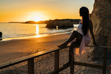 Woman sitting in a runway looking the sunset in the beach in Algarve, Portugal