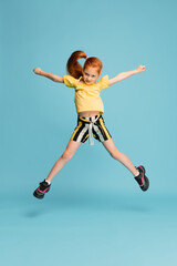 Fototapeta na wymiar Jumping high. Happy, smiley little caucasian girl isolated on blue studio background with copyspace for ad. Looks happy, cheerful. Childhood, education, human emotions, facial expression concept.