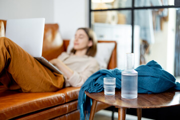 Obraz premium A glass jug of water on the coffee tables while pretty woman working on laptop and lying on sofa. Lifestyle and healthy concept. pitcher