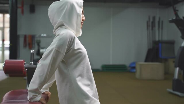 side view of an Arab woman, a Muslim woman with intense training, leaning on sports equipment, lifting her body and squatting. a Muslim woman in a hijab works out in the gym.