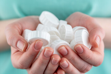 Hands are holding a handful of white plastic caps. Concept of environmental pollution, eco friendly behavior, waste sorting and plastic recycling. Closeup